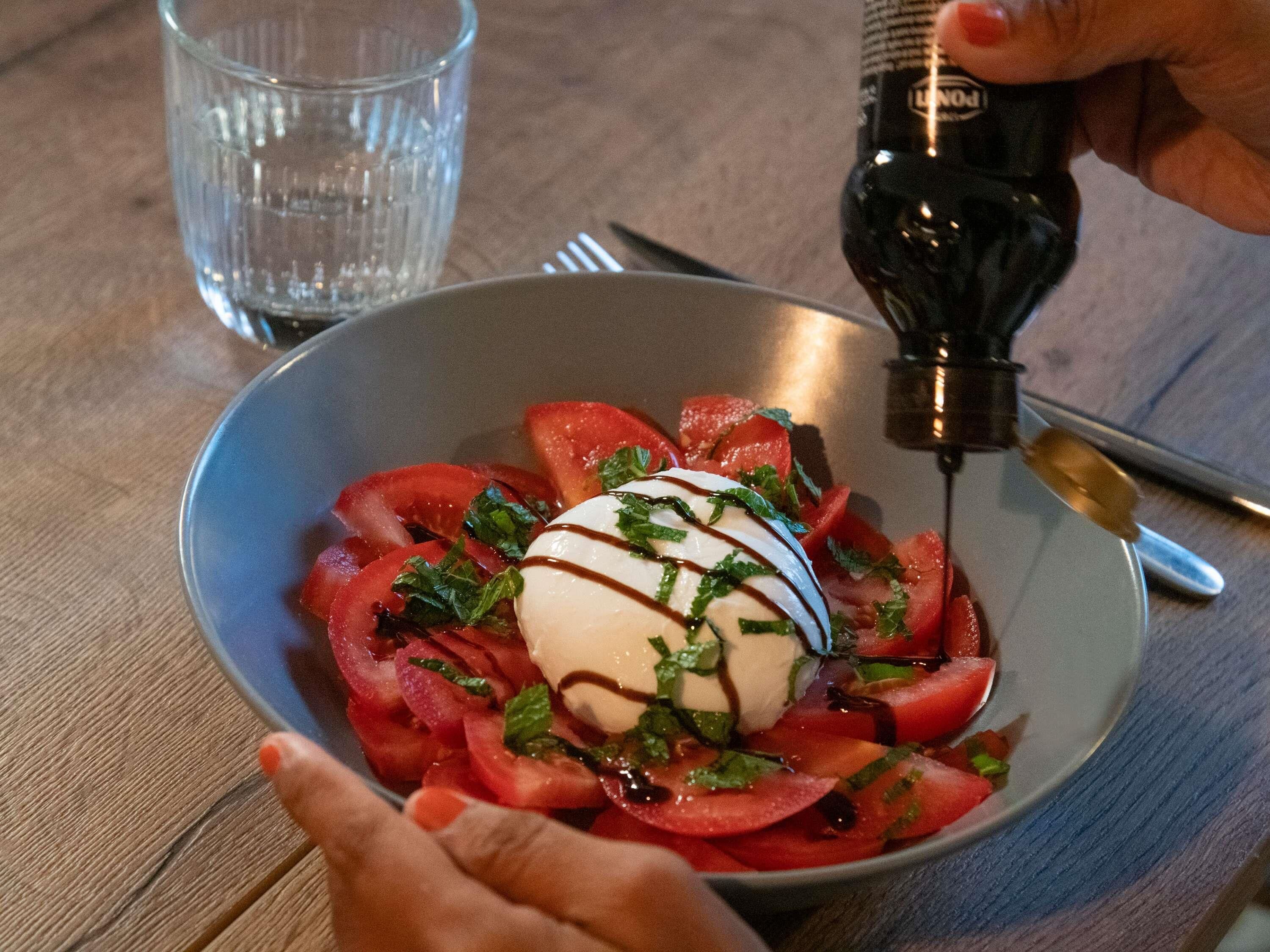 Eine Schüssel mit Essen, ein Klecks Sahne, ein Soßenüberzug, ein Glas Wasser und eine Soßenflasche auf einem Holztisch.