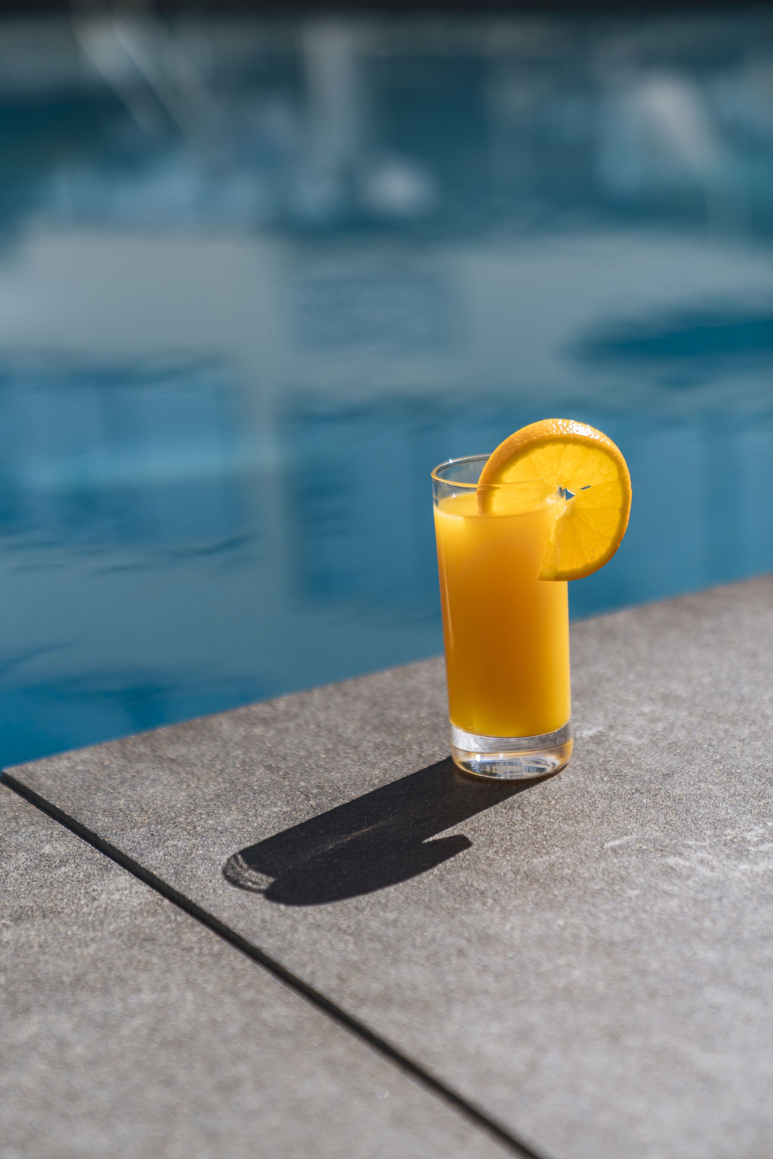 Un bicchiere di succo d'arancia con una fetta d'arancia su un tavolino a bordo piscina.