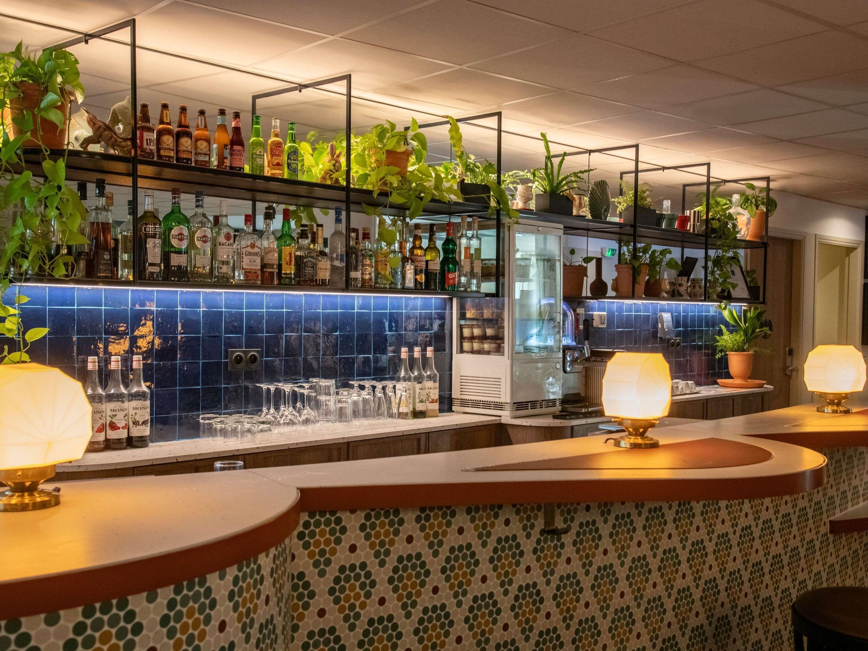A bar area with shelves of liquor bottles, a refrigerated display, and potted plants.