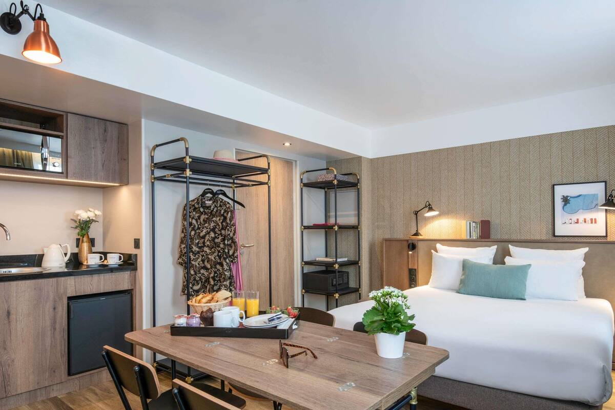 A compact hotel room with a bed, a small kitchenette, a dining area, and a bathroom.