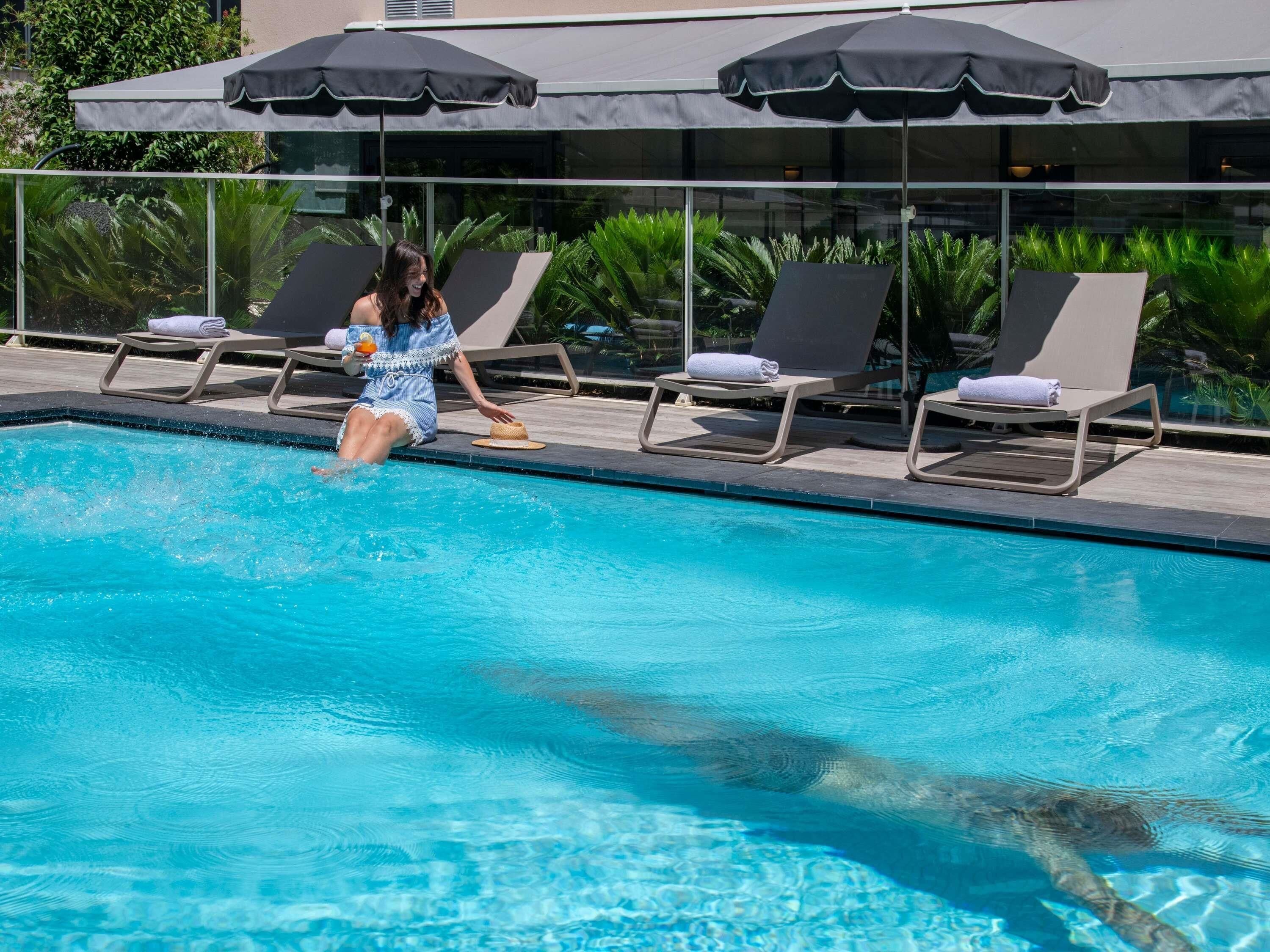 Una piscina al aire libre, sombrillas, sillones reclinables de piscina