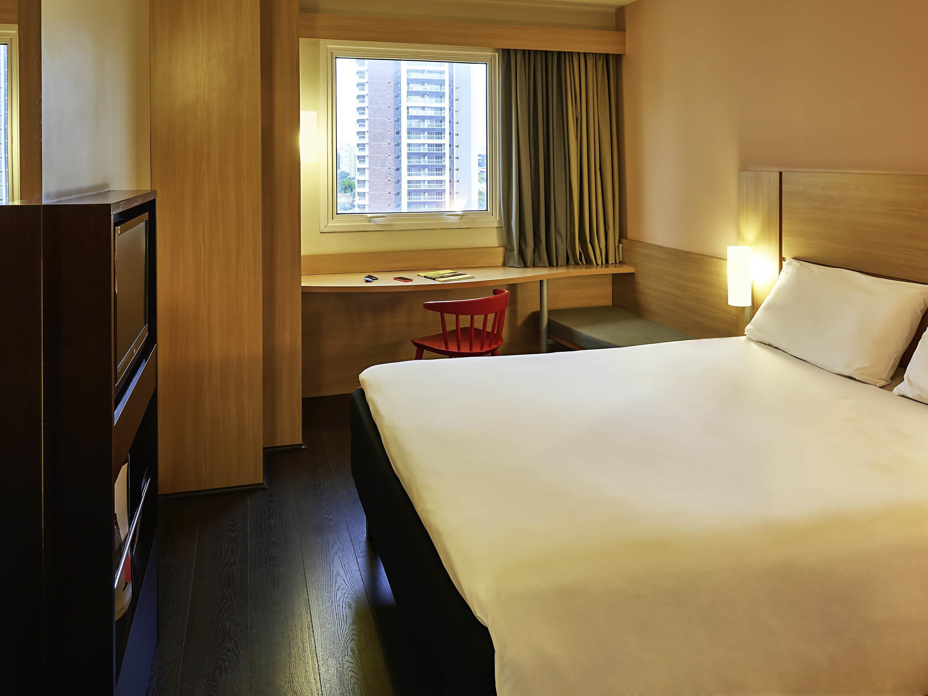 Een hotelkamer met een bed, bureau, stoel en een raam met gordijnen.