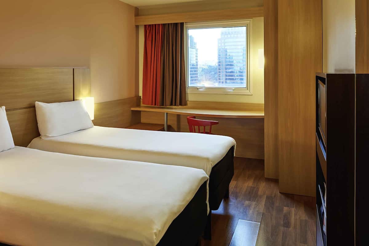Een hotelkamer met twee bedden, een bureau, een stoel, een televisie en een raam met gordijnen.