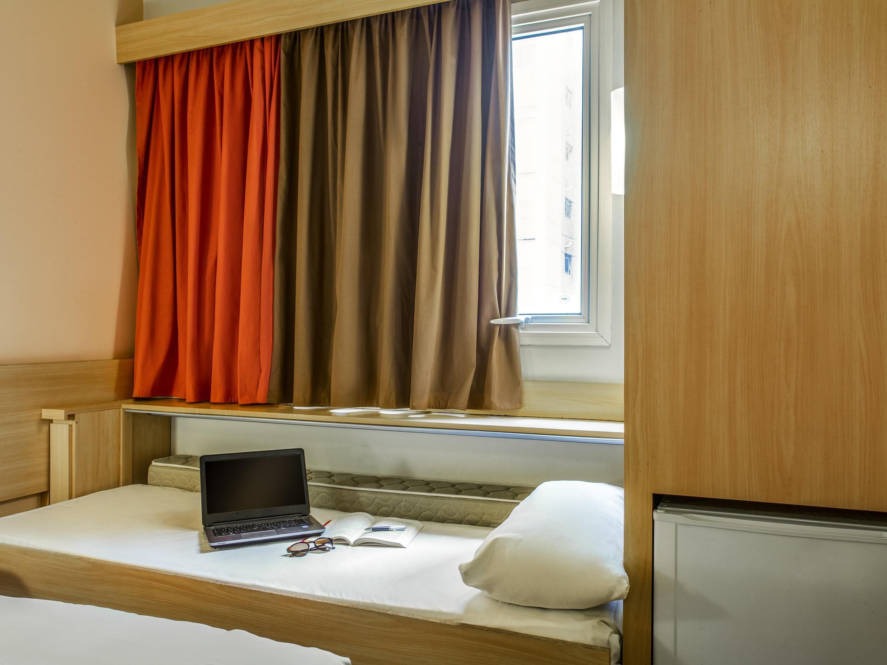 Una habitación con una cama, una computadora portátil, lentes y un libro abierto sobre la cama.