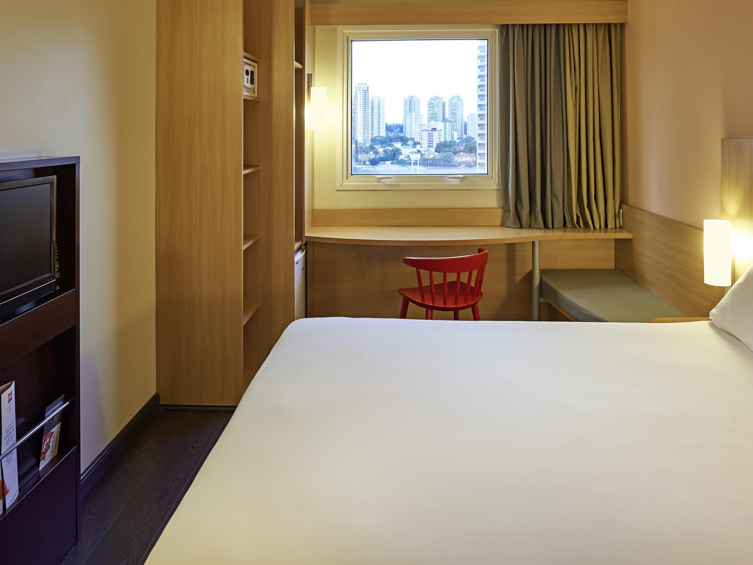 Habitación de hotel con cama, escritorio, silla, televisor y ventana con vista a la ciudad.