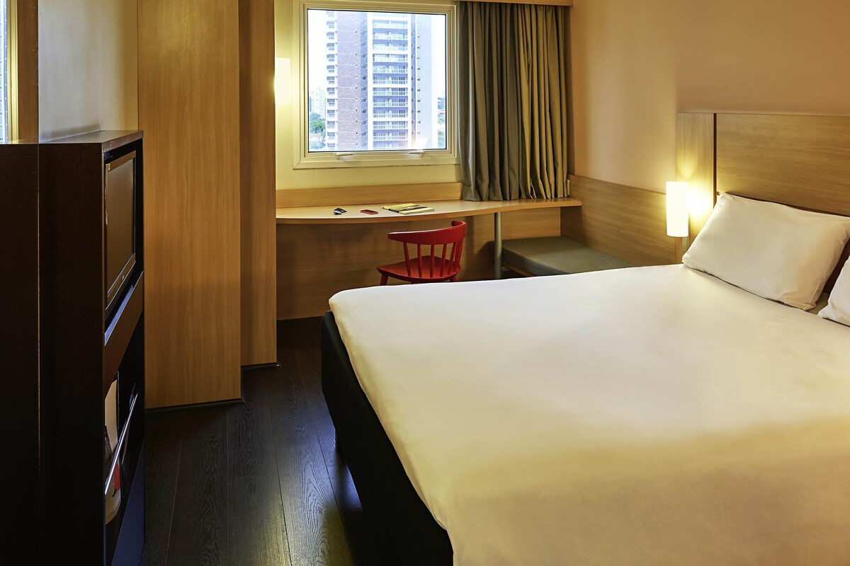 A hotel room with a bed, desk, chair, and a window with curtains.