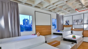 A modern hotel room with two beds, a large window with a city view, a wooden accent wall, and a ceiling with exposed beams.