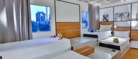 A modern hotel room with two beds, a large window with a city view, a wooden accent wall, and a ceiling with exposed beams.