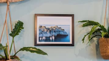 Fotografía enmarco de un litoral rocoso con barcos, colgada en una pared con dos macetas.