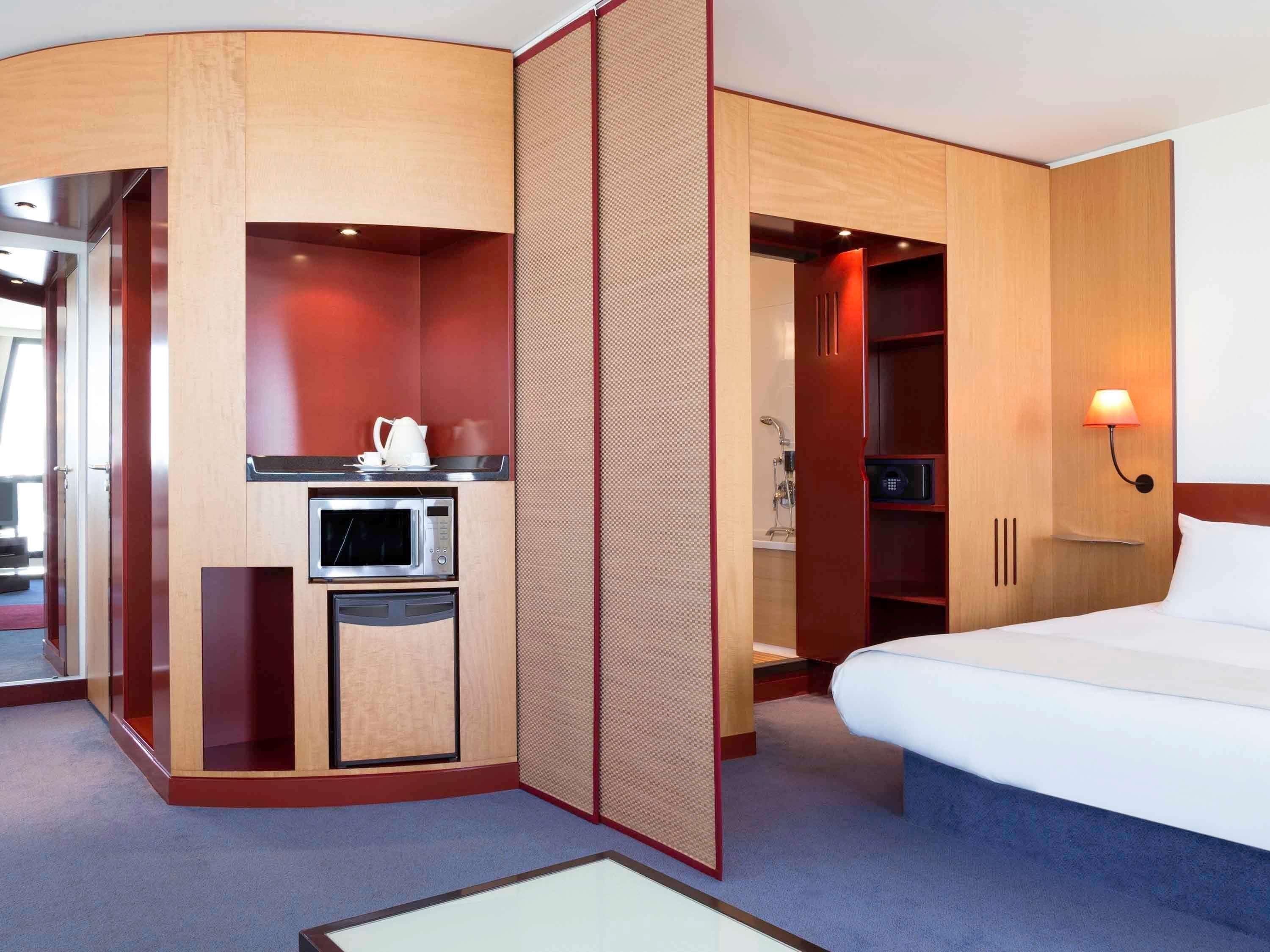 A hotel room with a bed, a microwave, a small refrigerator, a shower, and a seating area with a table.