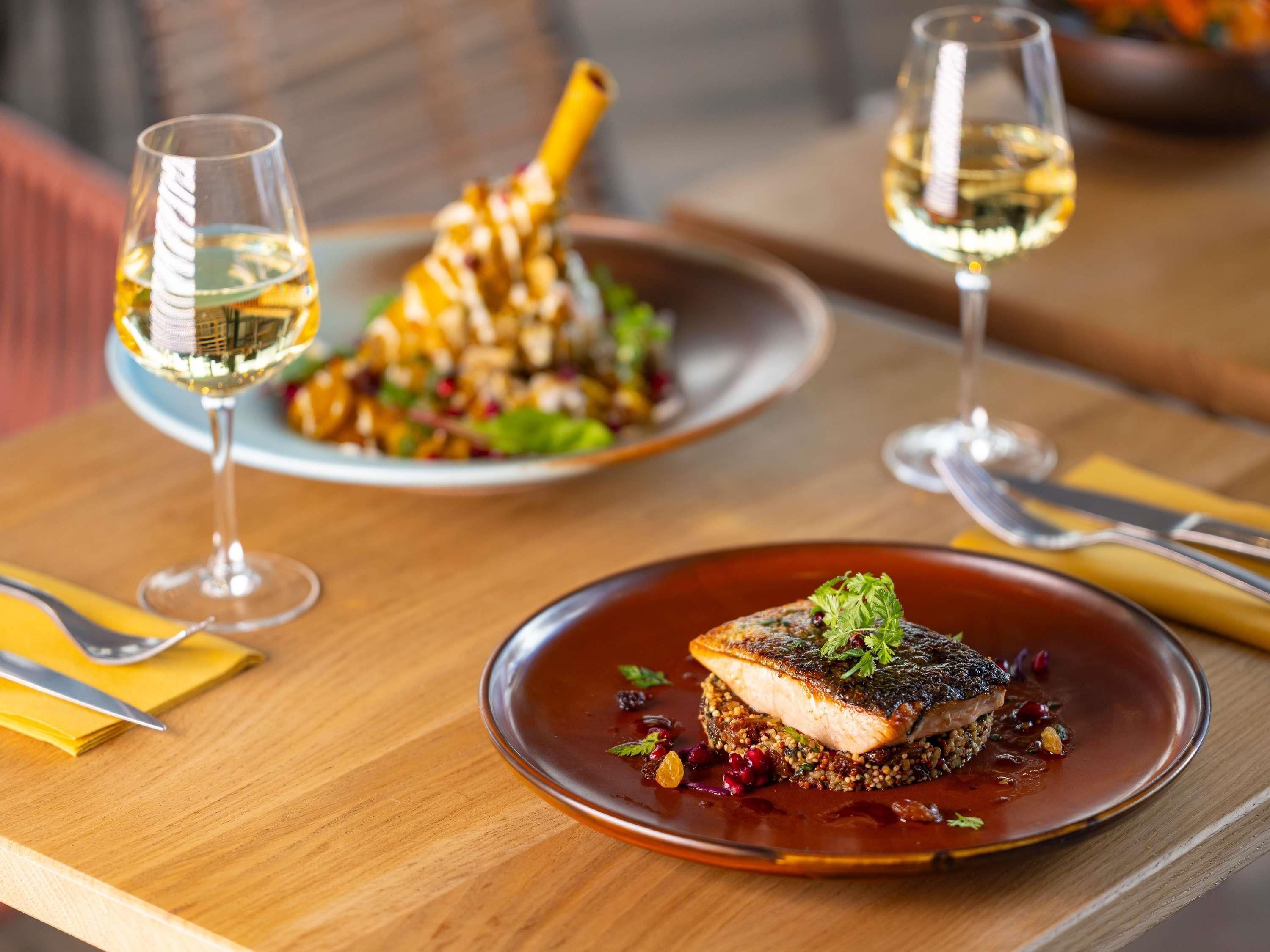 A dining table with plates of food and glasses of white wine.