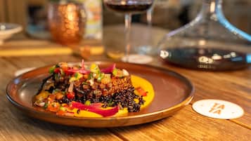 A dish with a variety of colorful toppings on a plate, accompanied by a glass of red wine and a decorative bottle on a wooden table.