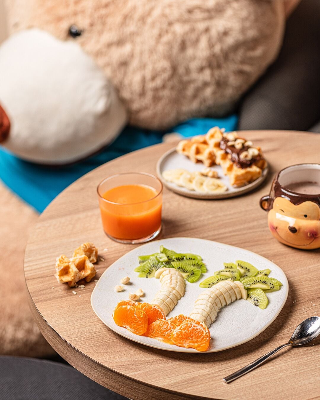 Uma mesa de madeira com uma travessa de frutas, um copo de suco de laranja e uma xícara de café.