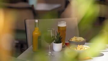 Uma mesa com uma garrafa, um copo, um vaso de planta e recipientes com petiscos.