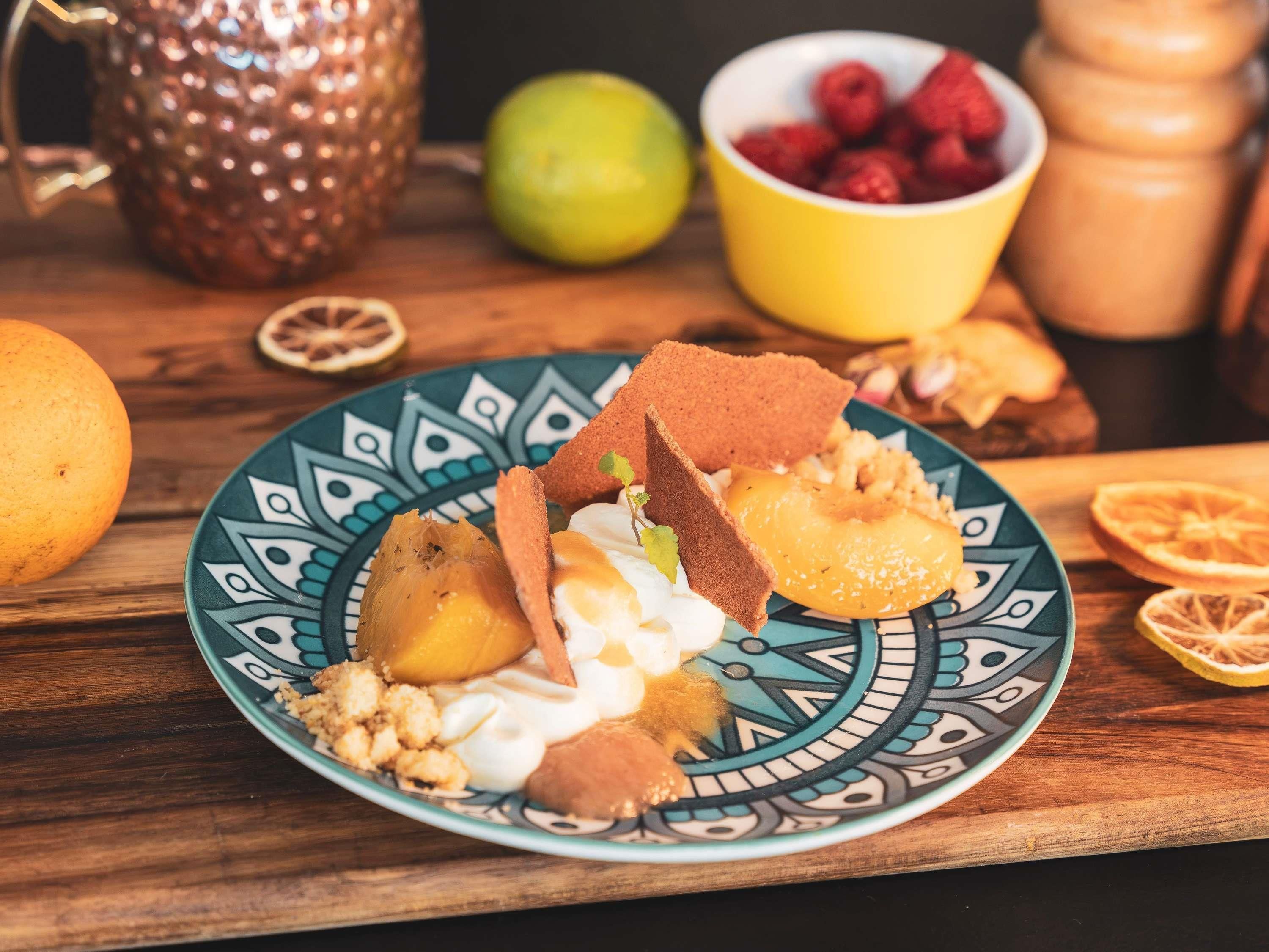 A plate with various food items, a copper pot, a bowl of berries, and a lemon on a wooden table.