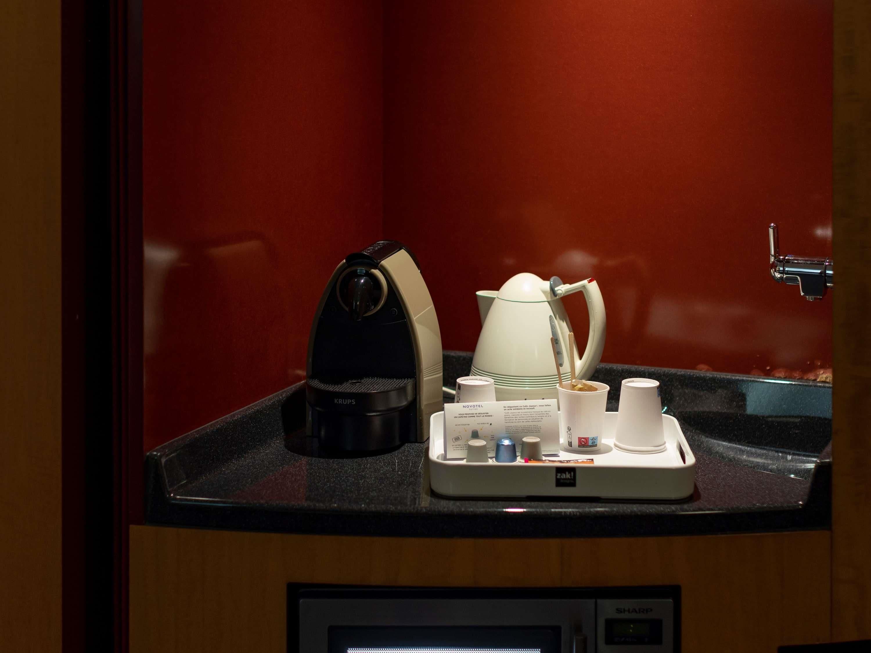 A coffee station with a coffee maker, a teapot, cups, and a tray with condiments.