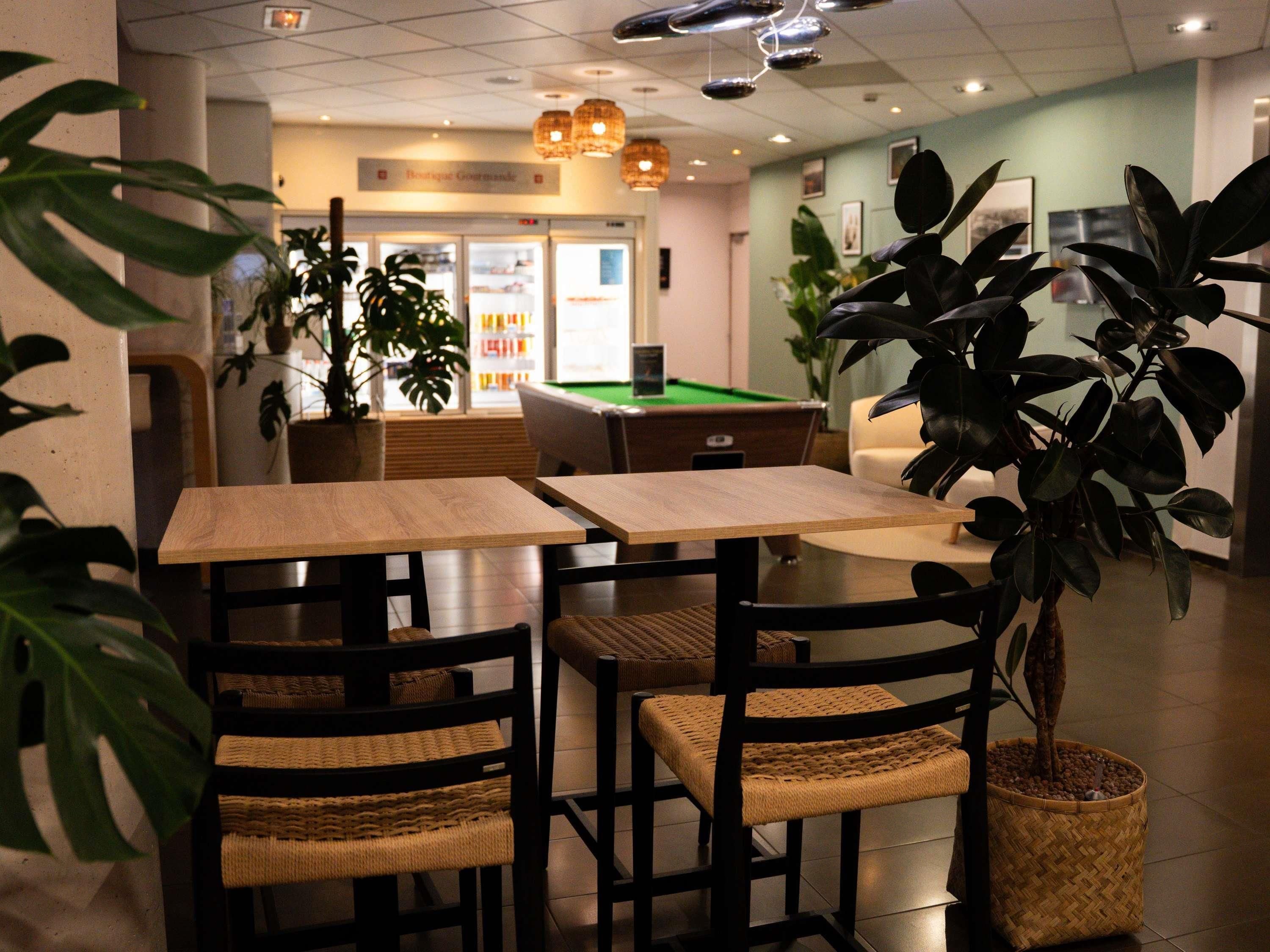 A restaurant with wooden tables and chairs, potted plants, and a pool table.