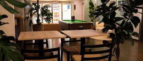 A restaurant with wooden tables and chairs, potted plants, and a pool table.