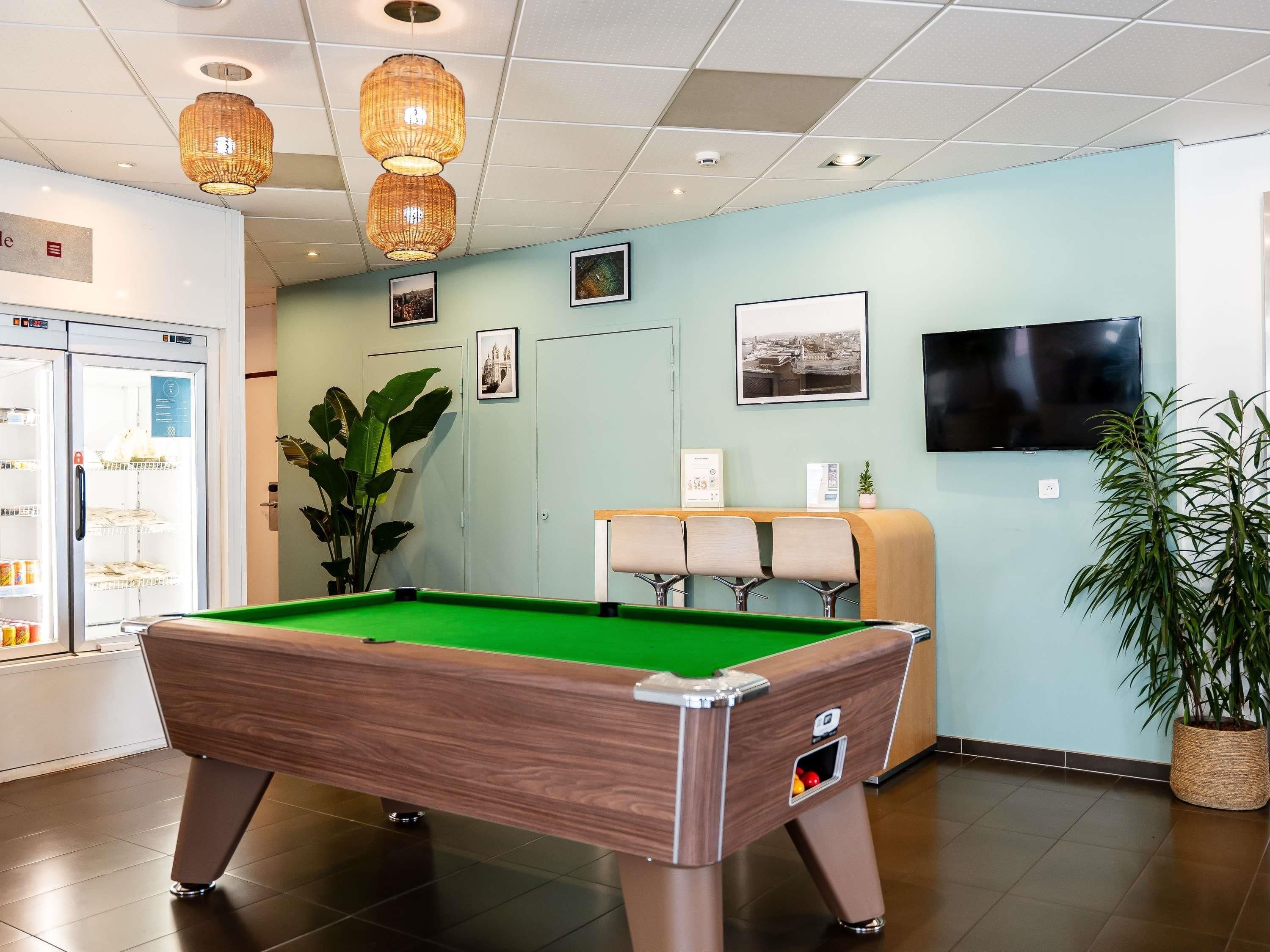 A pool table in a room with a refrigerator, a television, and framed pictures on the wall.