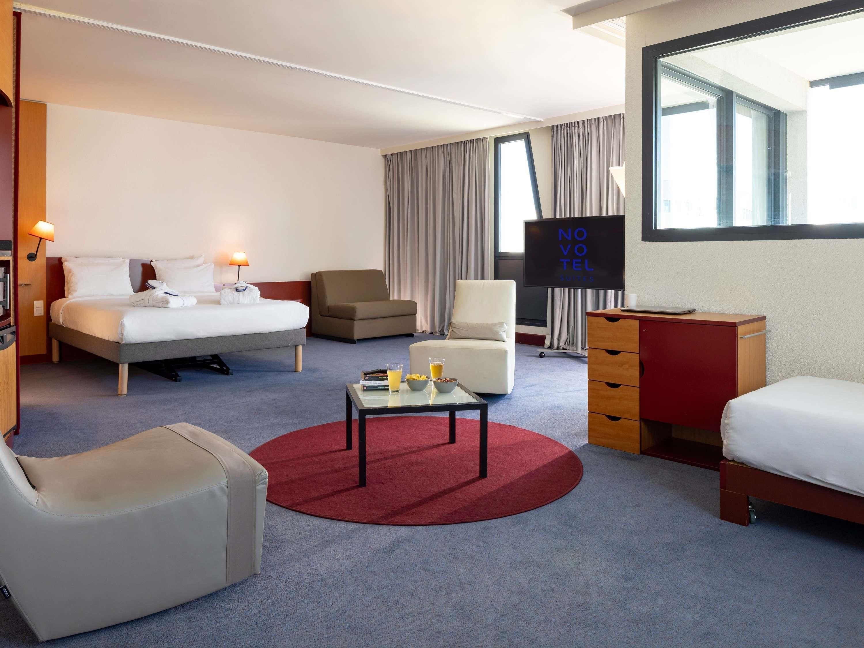 Habitació d'hotel amb un llit, dues butaques, escriptori, televisió i finestra amb cortines.