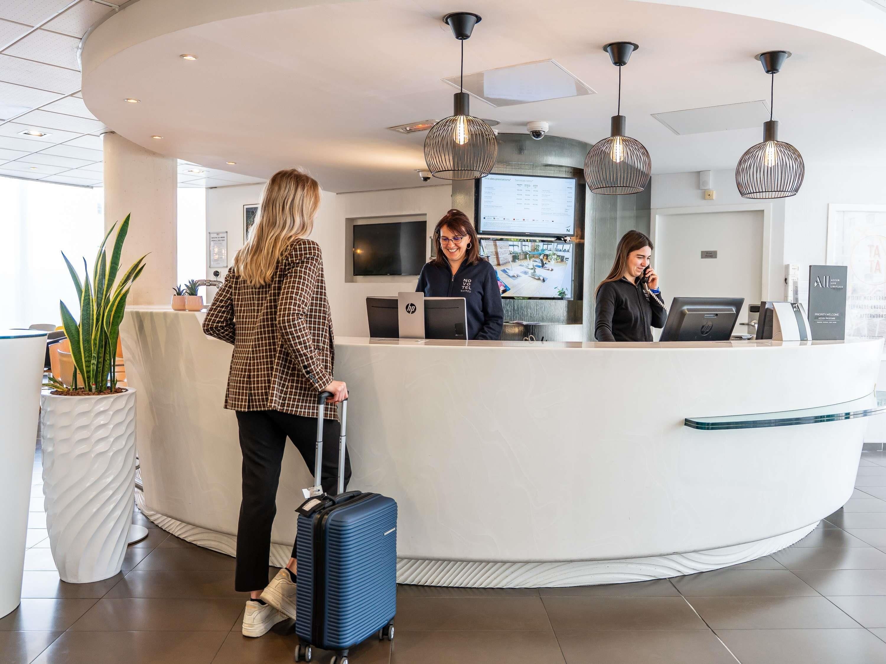 A hotel reception desk with a curved design, a large screen displaying information, and a security camera above.