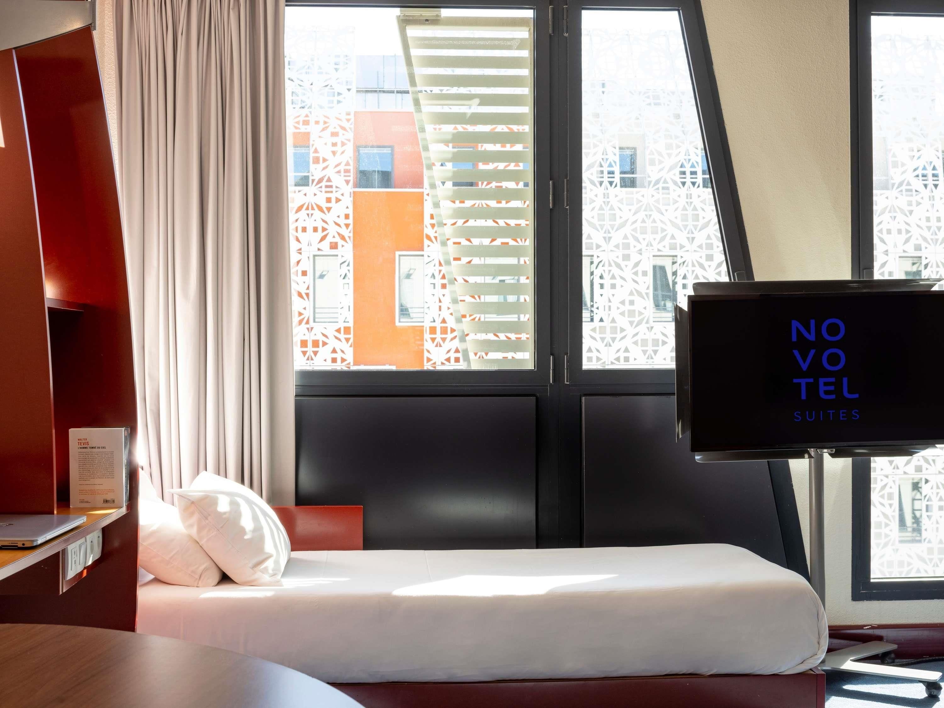 Quarto de hotel com cama, televisão e janela com vista para edifícios.