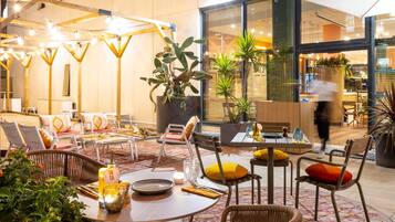 Een modern zithoek binnen met ronde tafels en rieten stoelen, met potplanten en sfeerverlichting.