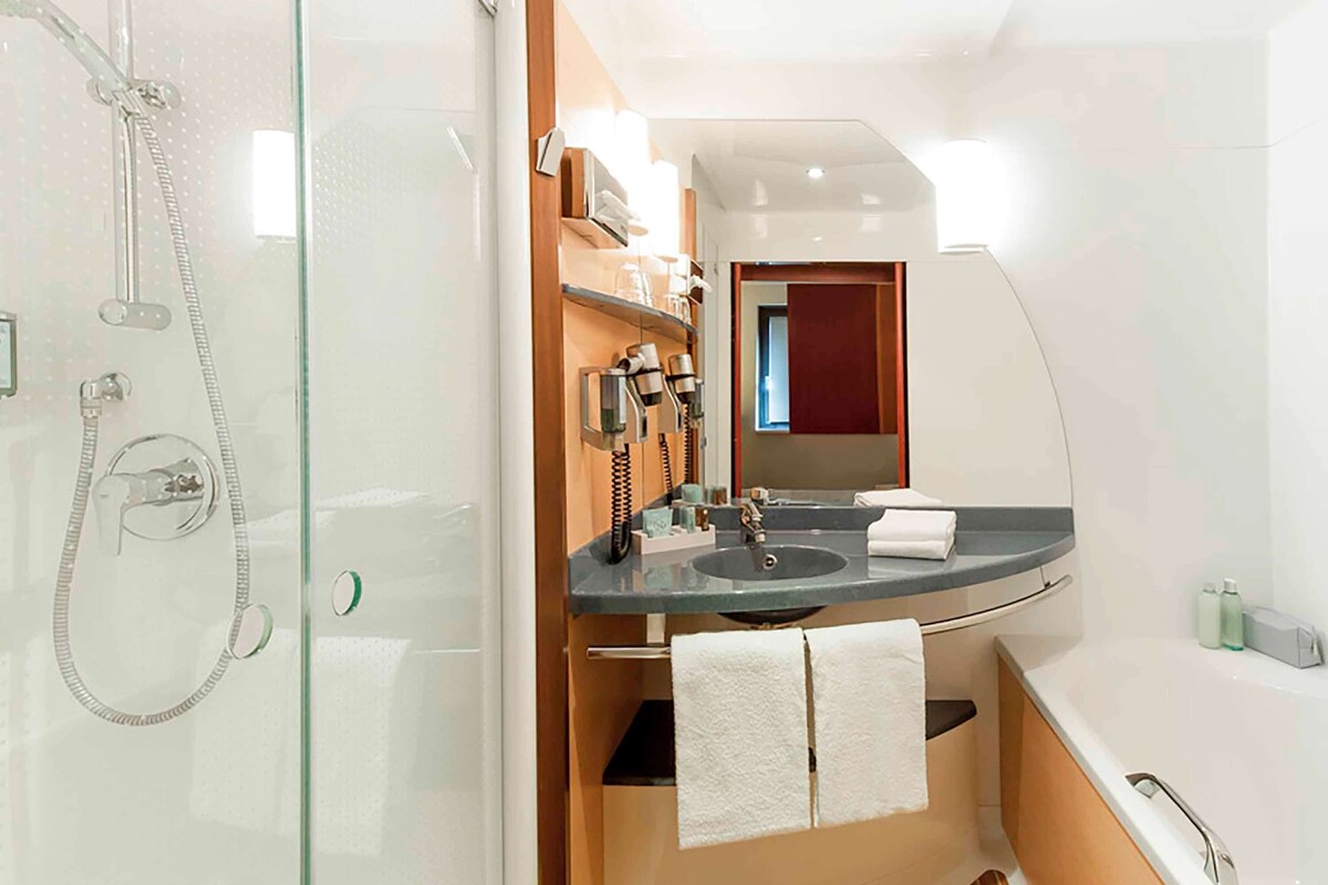 Un baño pequeño con ducha compartimentada por vidrio, tocador con lavamanos y espejo, y bañera.