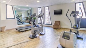 Un gimnasio con equipamiento de ejercicio, ventanas amplias y una televisión de pantalla plana.