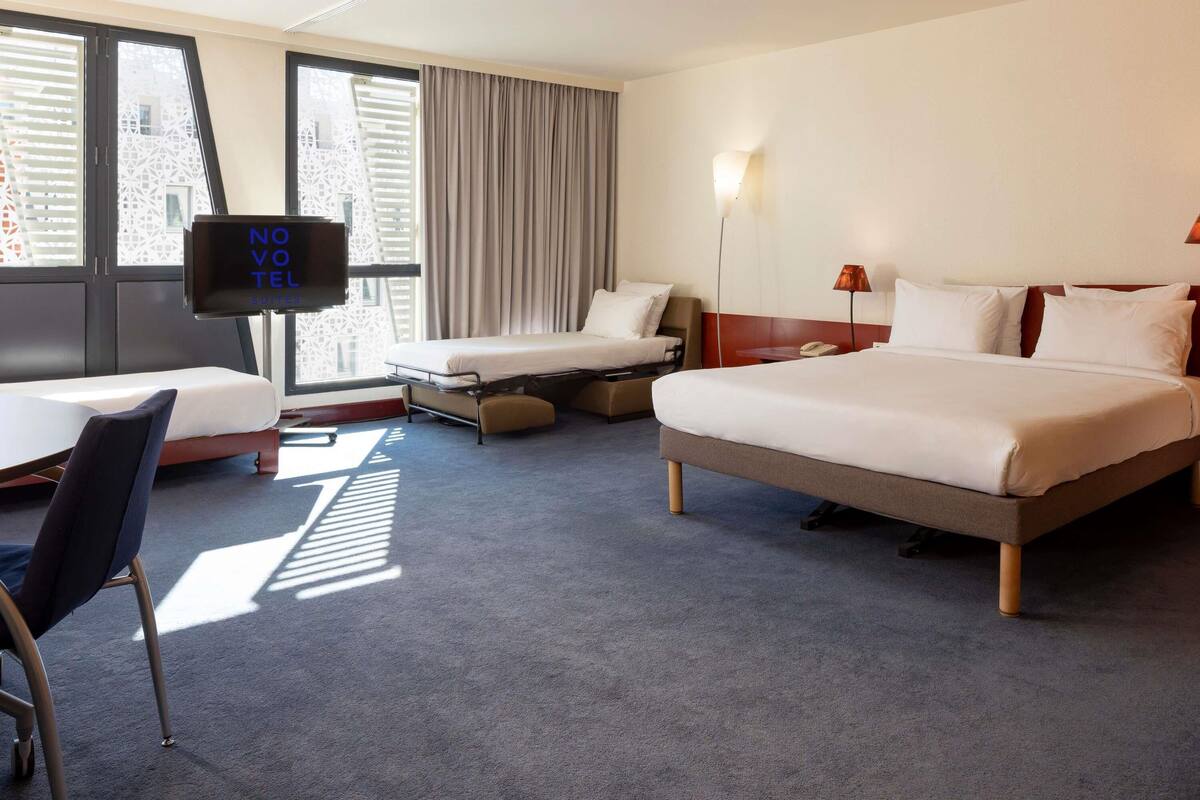 Ein Hotelzimmer mit Bett, Schreibtisch, Stuhl, Fernseher und einem Fenster mit Vorhängen.