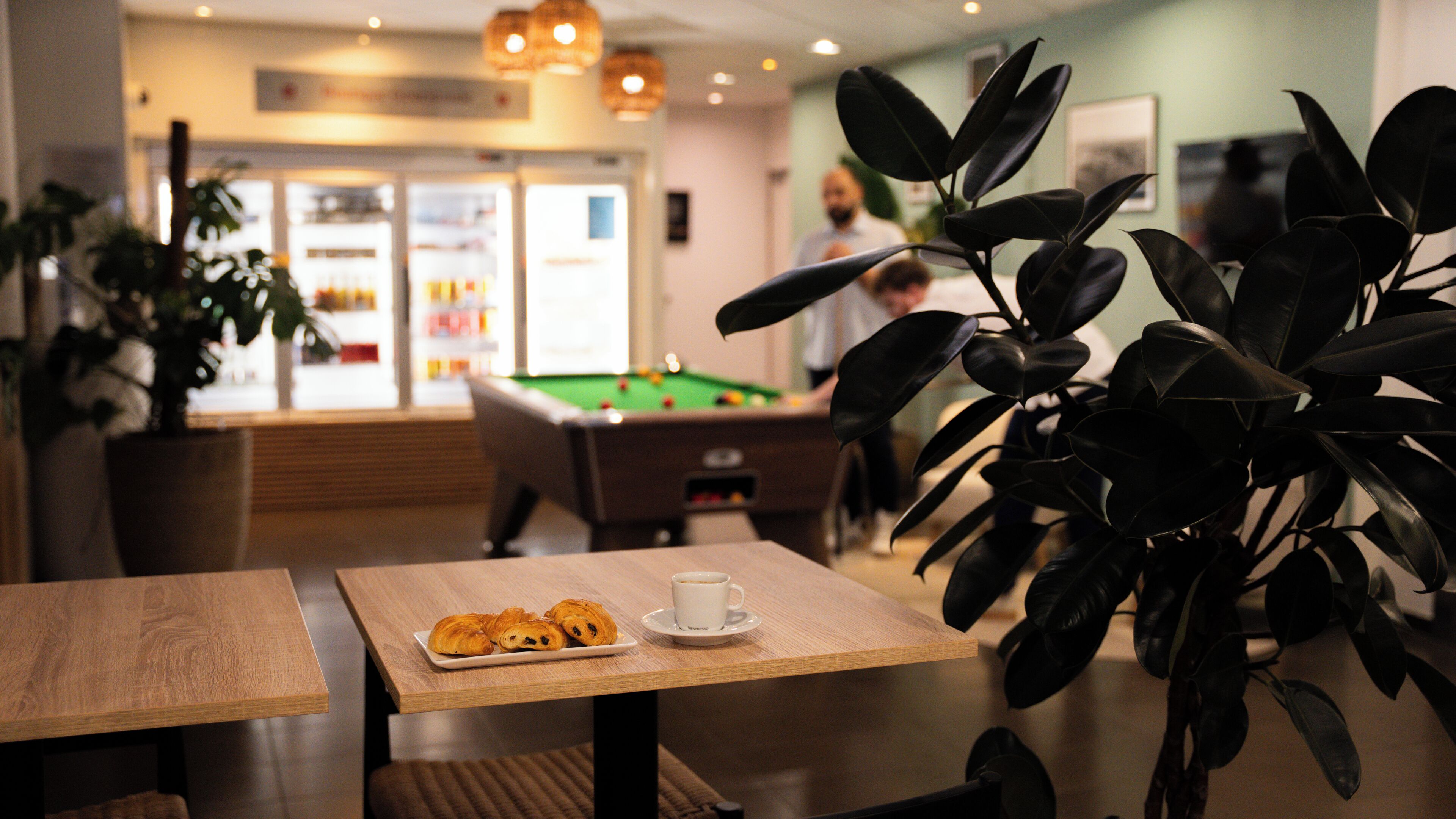 Un espace intérieur accueillant avec une table de billard, une table basse sur laquelle sont disposées des pâtisseries et une plante en pot.