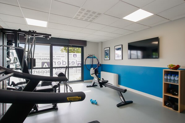 A gym with exercise equipment, a TV, and a water bottle shelf. - Clarion Aparthotel Toulouse Blagnac Airport (Blagnac)