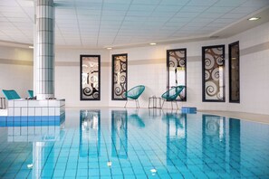 Ein Schwimmbecken mit klaren blauen Fliesen, umgeben von Wänden mit dekorativen Verzierungen und einigen Liegestühlen.