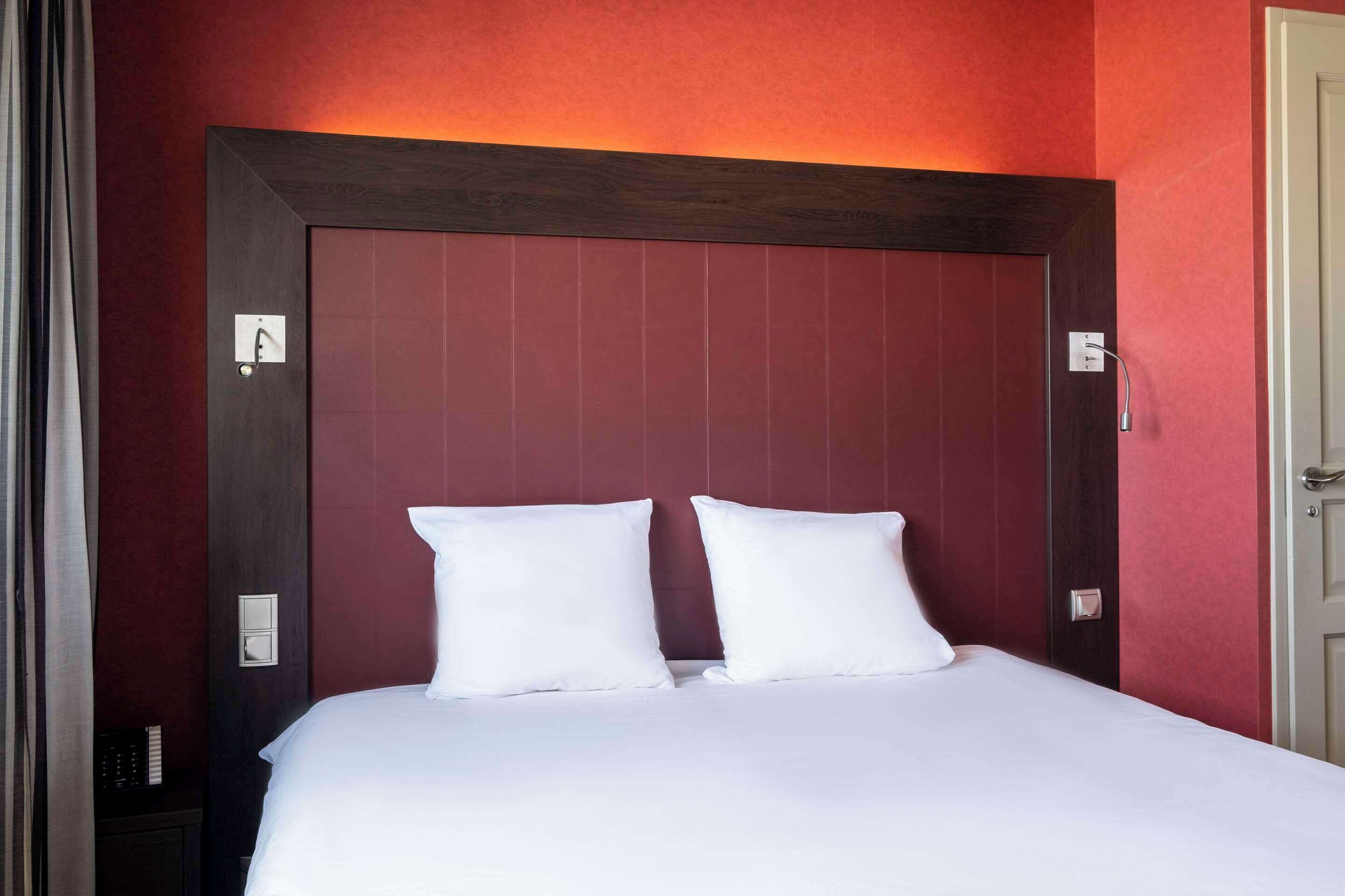 Una habitación de hotel con una cama grande, un cabecero de madera oscura y paredes rojas.