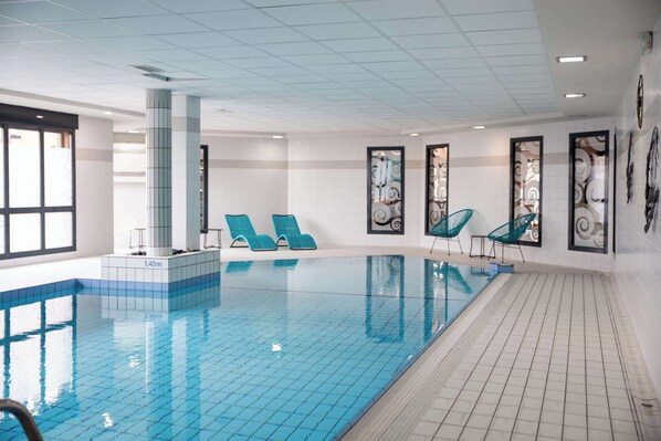 Ein Swimmingpool mit blauen Fliesen, einer gefliesten Liegefläche und vier türkisblauen Liegestühlen.
