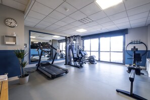 Un gimnasio con cinta de correr, máquinas de pesas y un amplio ventanal.