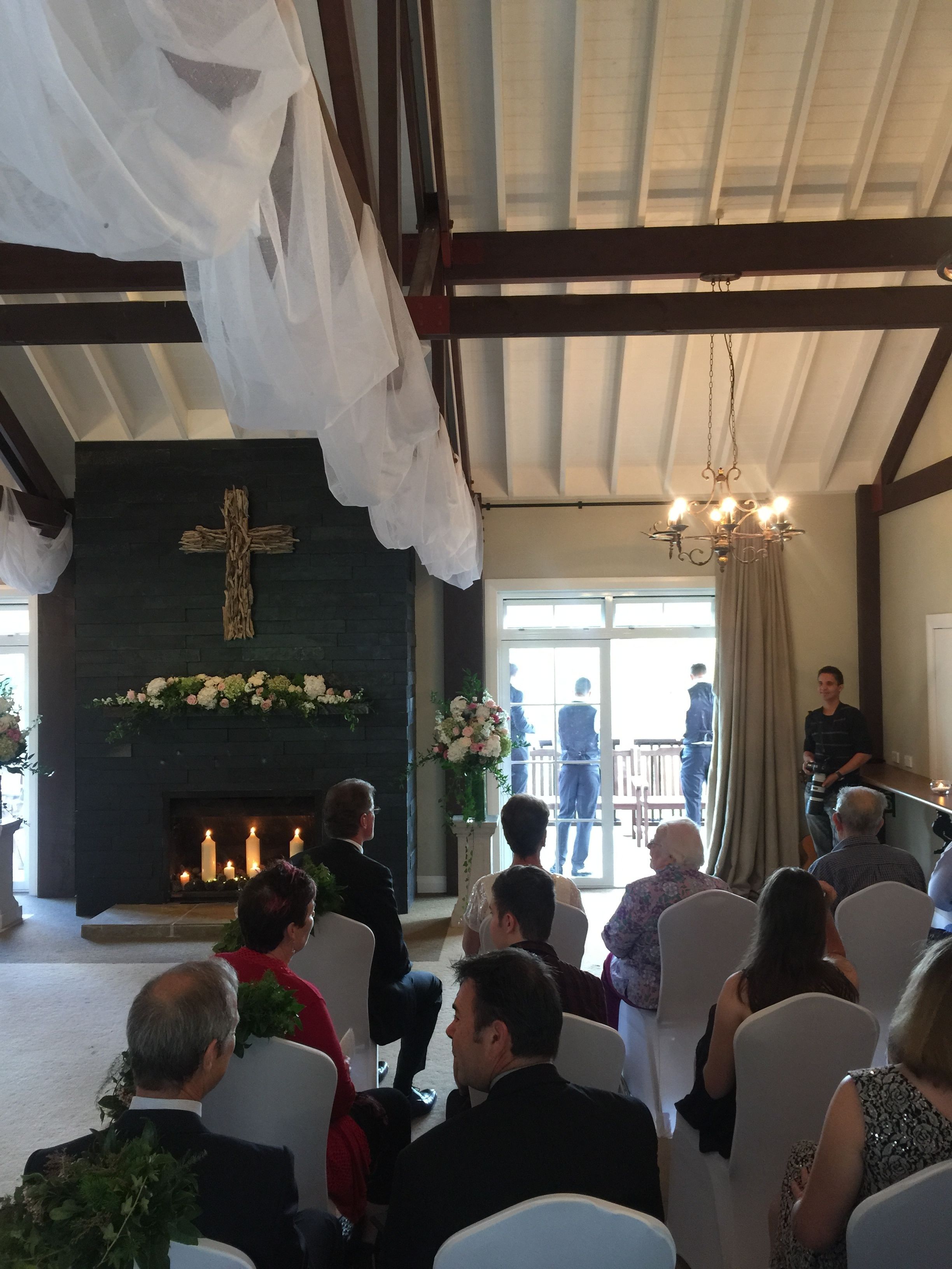 A church interior with pews, a cross on the wall, a fireplace, and a chandelier.