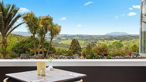 A dining table with a menu, a glass, and a vase with a plant, overlooking a scenic landscape with trees and hills. - Woodhouse Mountain Lodge (Warkworth)