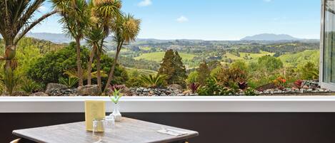 Una mesa de comedor con un menú, un vaso y un florero con una planta, con vistas a un paisaje pintoresco con árboles y colinas.