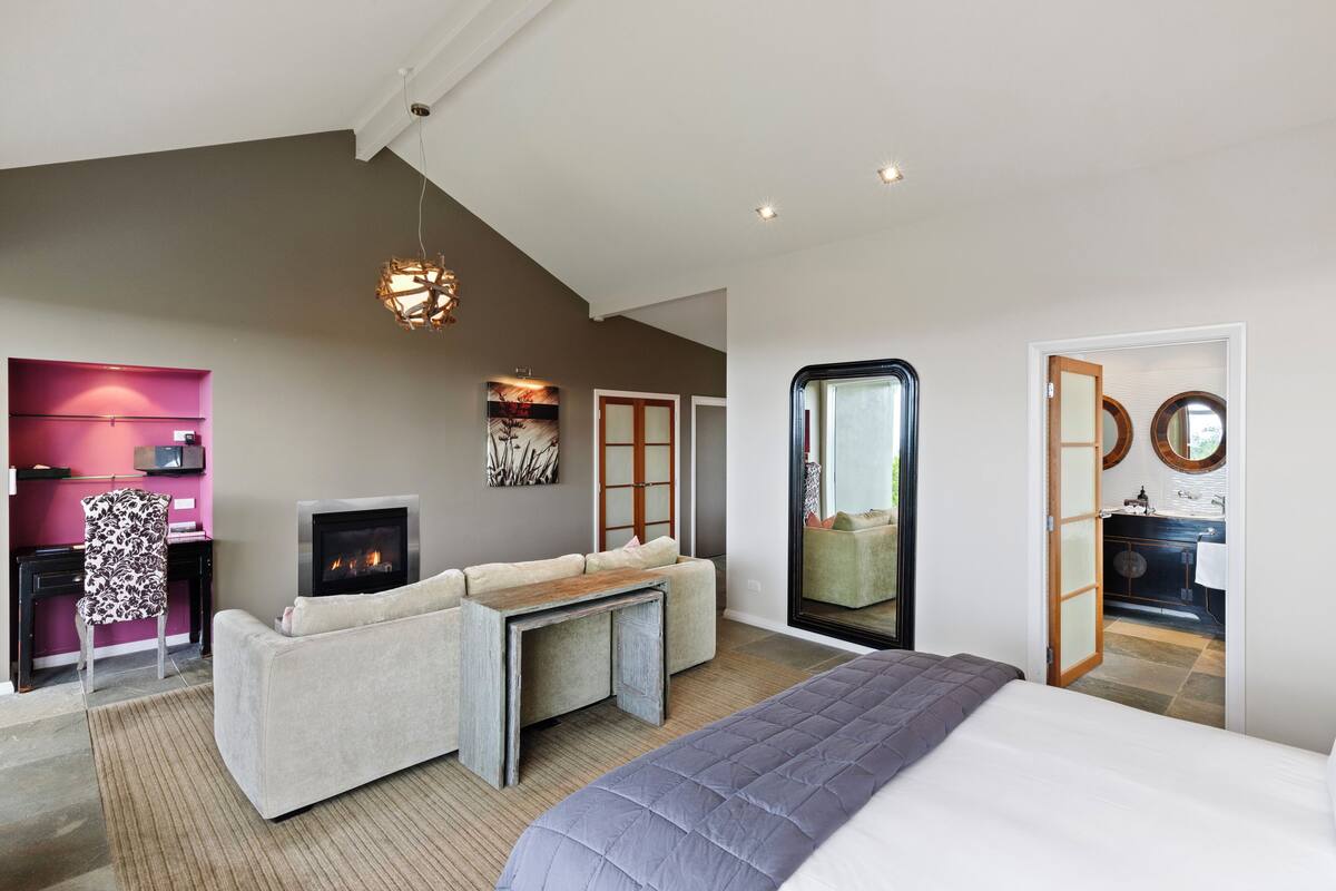 Une chambre moderne avec un grand lit, un canapé, une cheminée et un coin repas.
