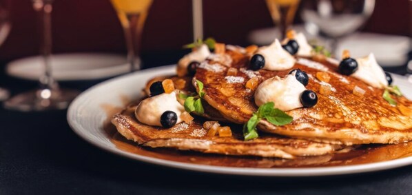 A plate of pancakes with whipped cream, blueberries, and a syrupy sauce. - Agua Caliente Casino Rancho Mirage (Rancho Mirage)