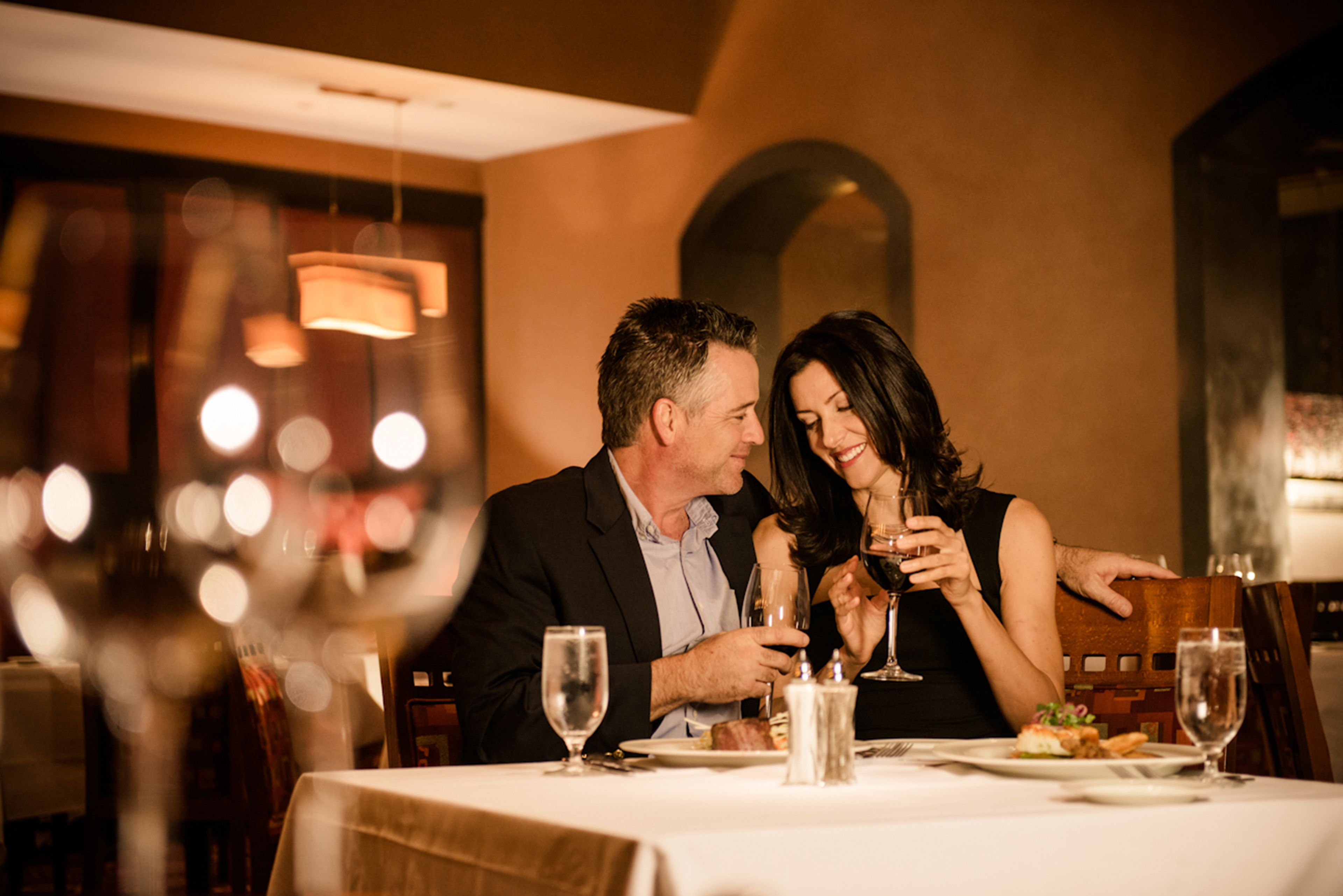 A couple dining at a restaurant with a table set for two, wine glasses, and a candle on the table.
