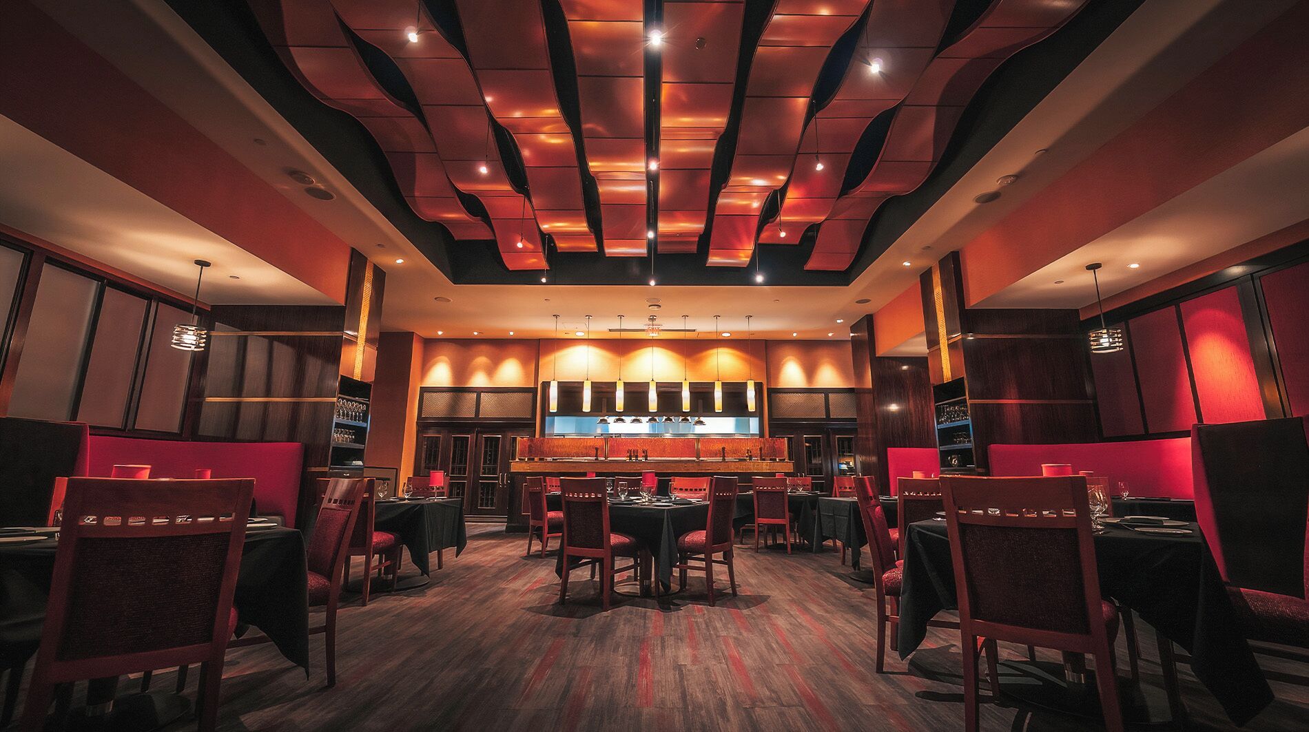 Un restaurante con una decoración moderna, que presenta una barra central, diversas opciones de asientos y un diseño de techo distintivo.