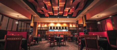 Un restaurante con una decoración moderna, que presenta una barra central, diversas opciones de asientos y un diseño de techo distintivo.