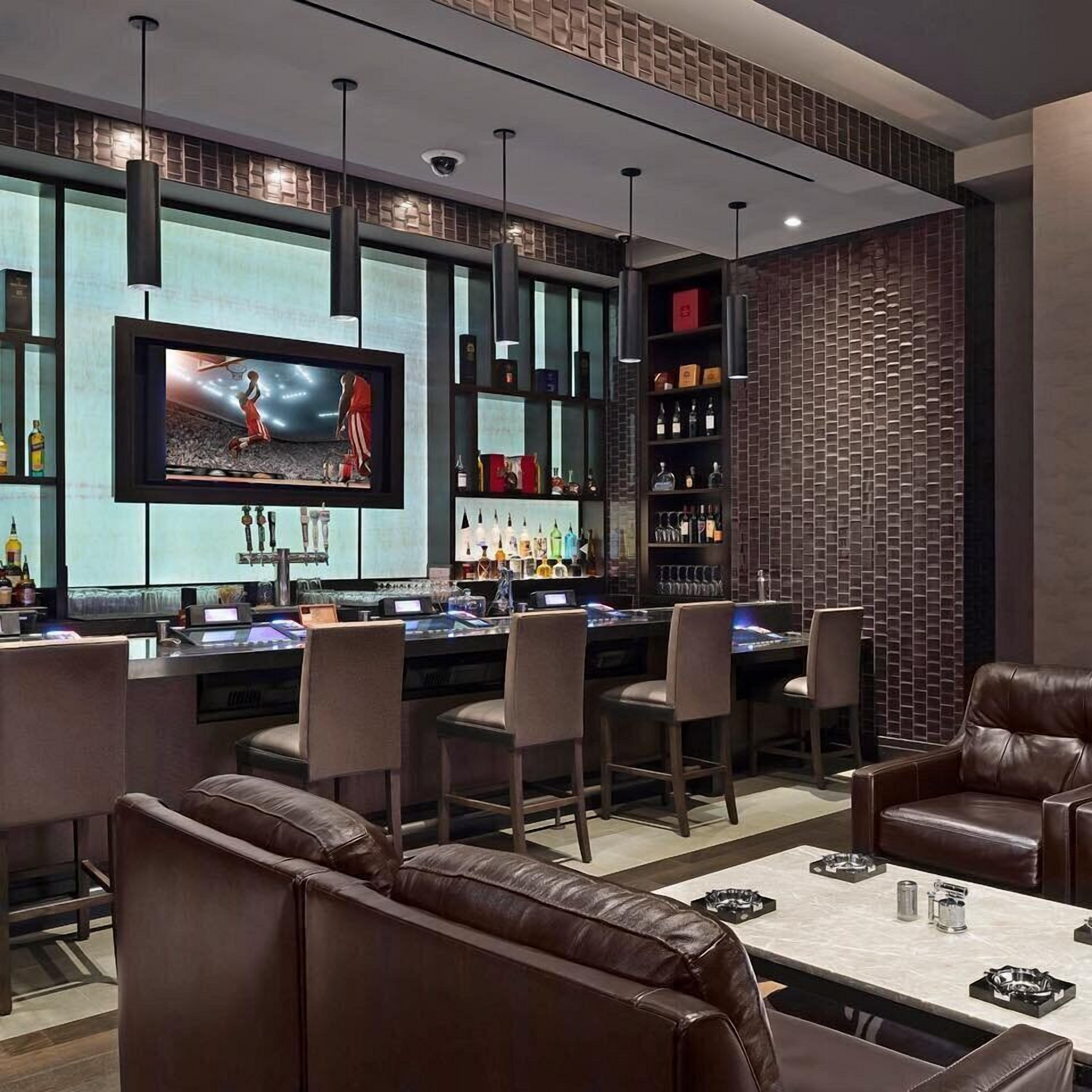 Zona de bar com assentos de couro, uma tela de televisão e prateleiras com garrafas.