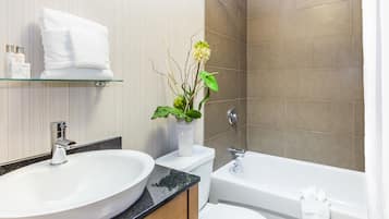 A bathroom with a white sink, toilet, and bathtub. There is a glass shelf above the sink holding a white towel and a vase with flowers.