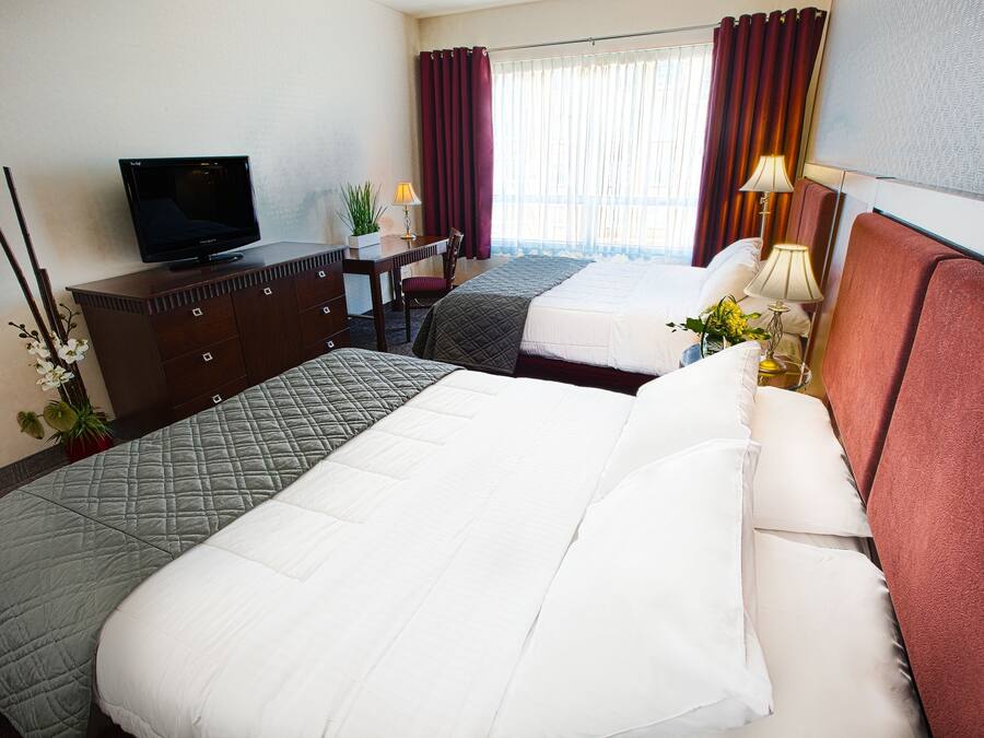 Una habitación de hotel con dos camas, un televisor, un escritorio y una ventana con cortinas.