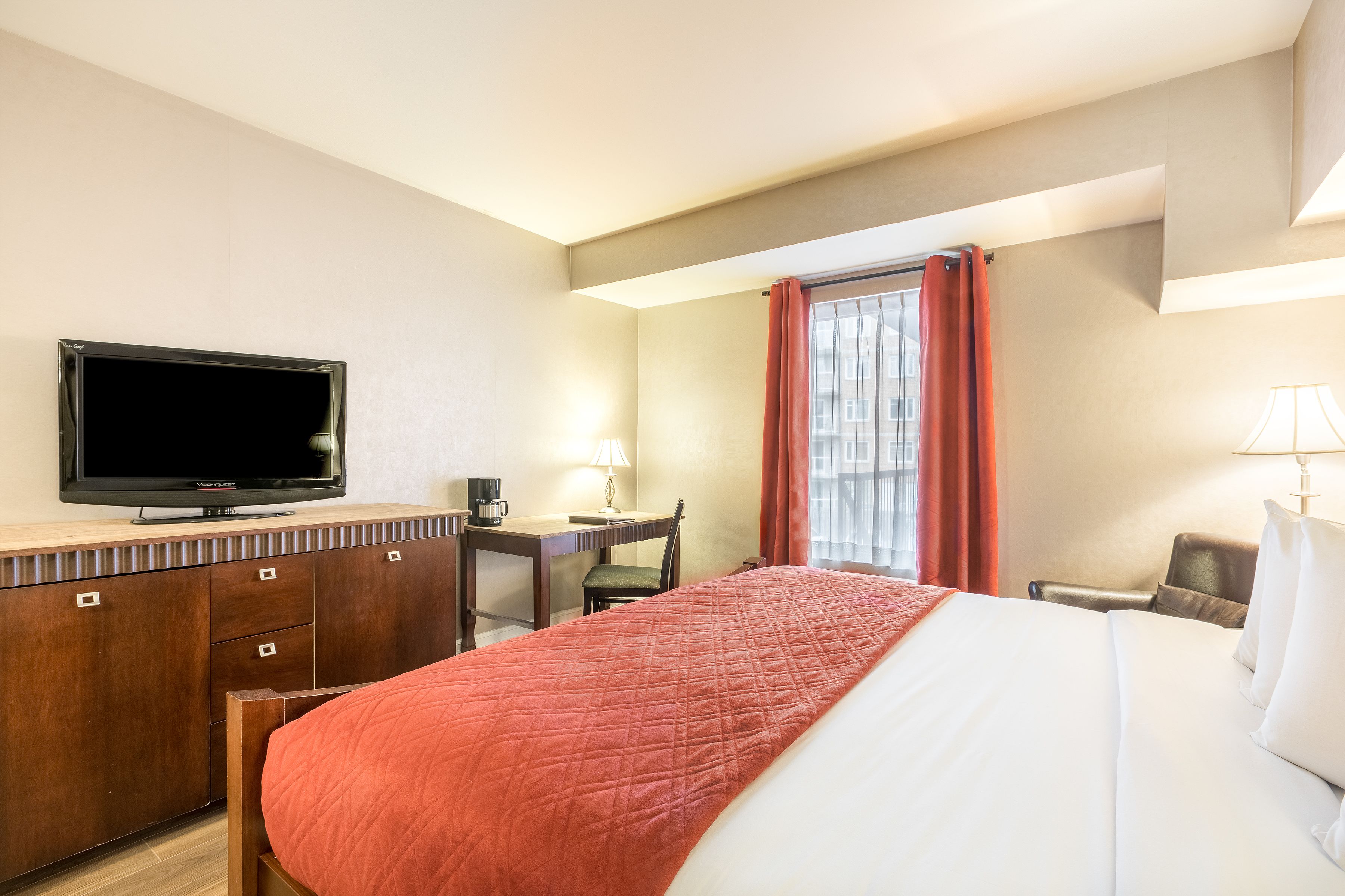 Quarto de hotel com cama, escrivaninha, televisão e janela com cortinas.