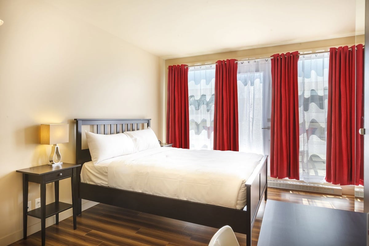 A hotel room with a bed, bedside table, lamp, and a view through the window.
