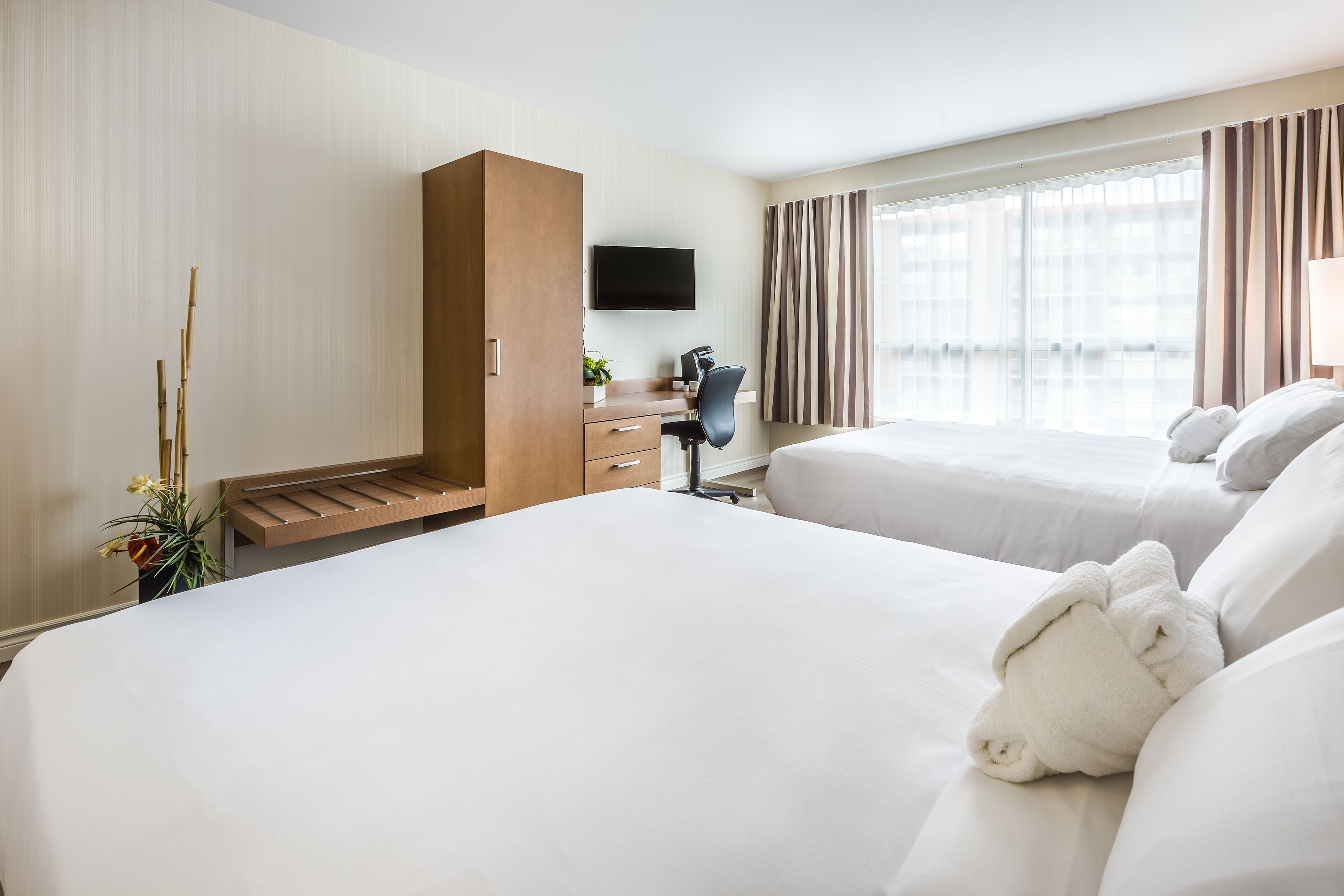 A hotel room with two beds, a desk with a chair, a TV, and a window with curtains.